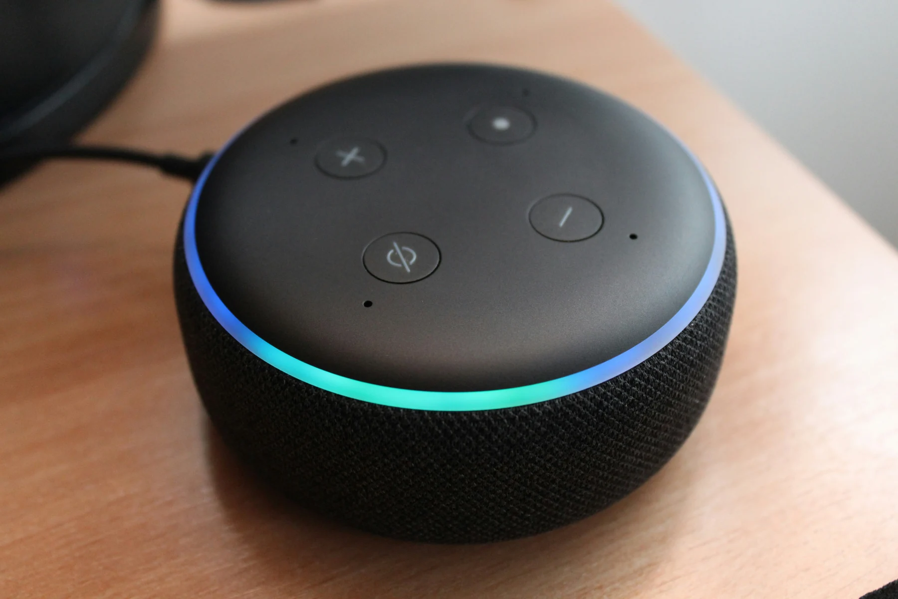 Voice assistant speaker with an illuminated blue and turquoise ring on a wooden desk